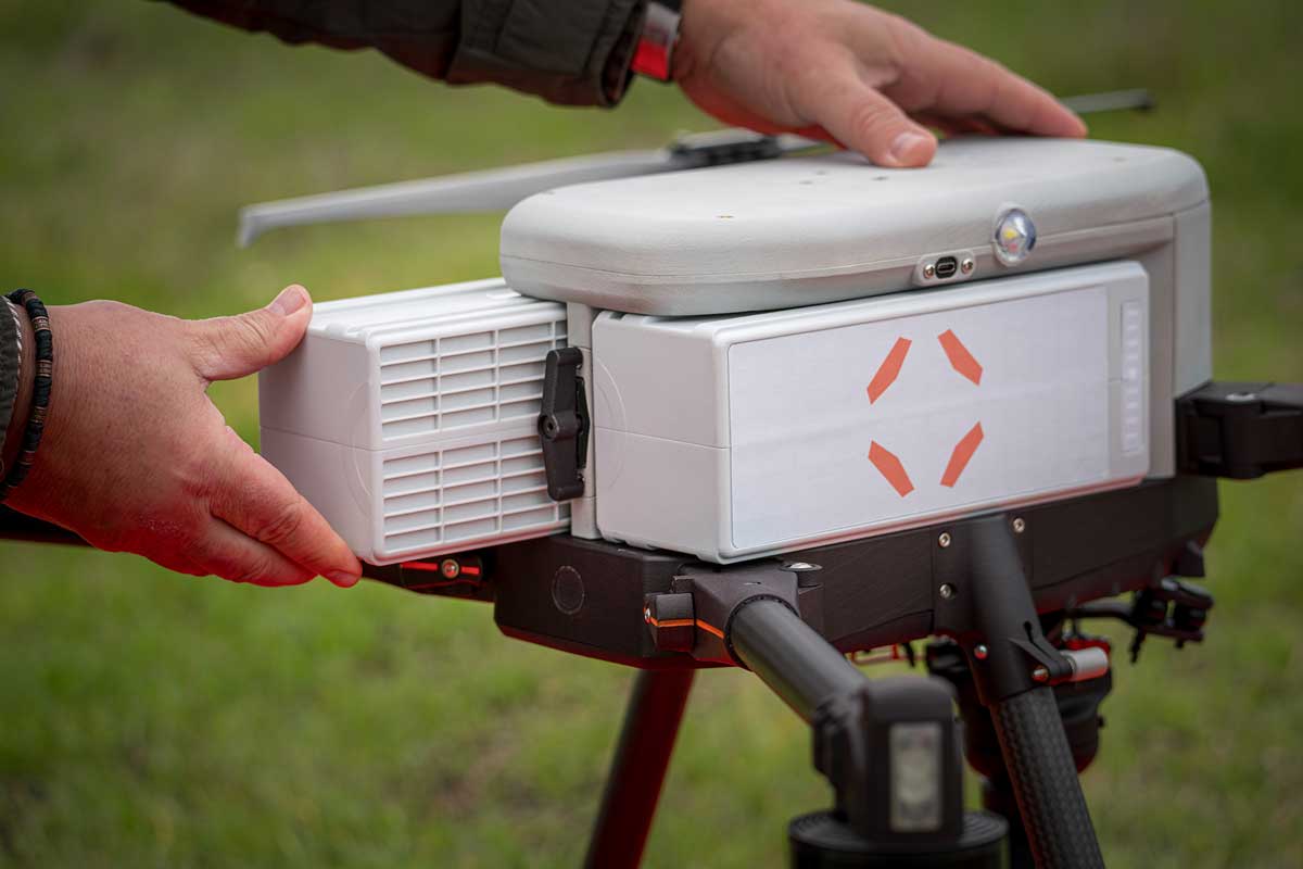 A close-up of a hot swappable police drone batteries being inserted into IF800 tomcat drone with a person's hands adjusting or securing the top cover outdoors on a grassy background.