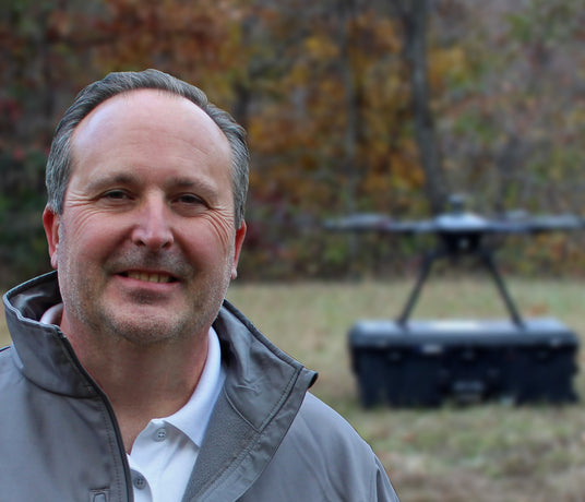 Man standing outdoors with a blurred background of trees and drone