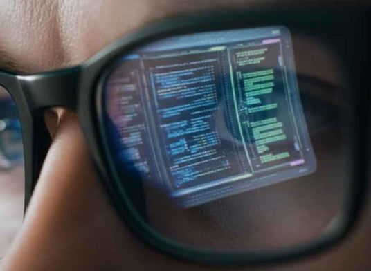 Person wearing glasses with computer code reflected on the lenses