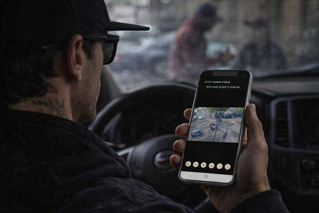 Person inside a vehicle holding a smartphone with an app open, showing a map or navigation interface.