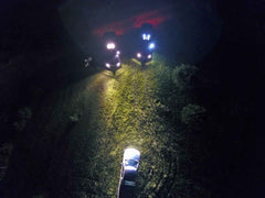 Three vehicles on a dark road at night with headlights illuminating the path.