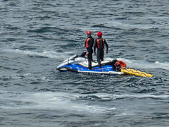 Two people on a jet ski in the water, wearing life vests and helmets.