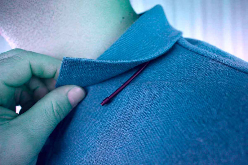 Close-up of a hand sewing a blue garment with a needle and thread.