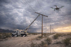 Drones inspecting power lines in a desert landscape with a truck and crane in the foreground.