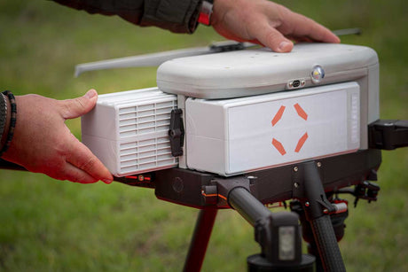 A close-up of a hot swappable police drone batteries being inserted into IF800 tomcat drone with a person's hands adjusting or securing the top cover outdoors on a grassy background.