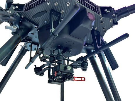 Close-up of a black quadcopter drone's underside and landing gear, featuring a mounted camera gimbal with a red handle, on a white background.
