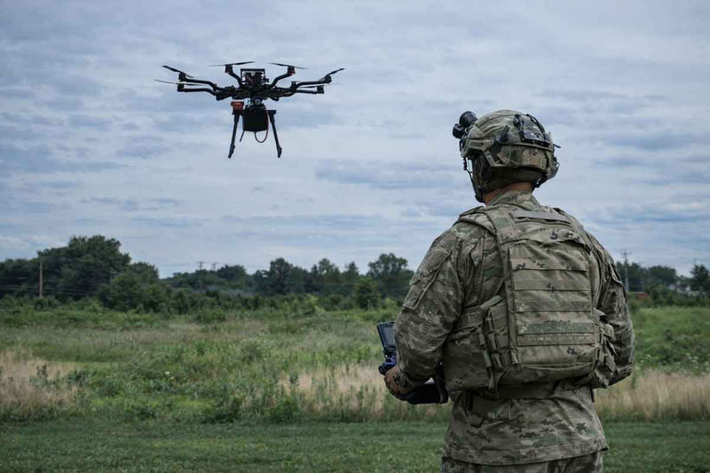 Person in military uniform operating a drone in an open field