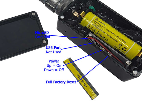 A close-up of a black undercover body wire  device showing its internal components, with a yellow cylindrical battery and a yellow USB-C cable. Blue text labels point out features such as the microSD card slot, unused USB port, power up/down, and factory reset.