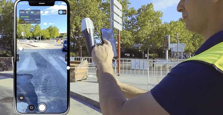 A person outdoors holding a tablet and a smartphone, with a large phone screen overlay showing a street scene. Trees, a sidewalk, and urban background are visible.