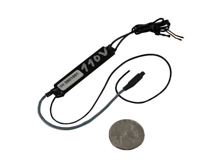 A small black wireless covert audio bug with attached wires and a coin placed below it for scale, photographed on a plain white background.