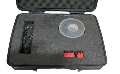 An open black hard carrying case with custom foam inserts, containing a clear plastic round container, a coiled black cable or tube, covert audio bug listening device and two small red-and-orange accessories, shown on a white background.