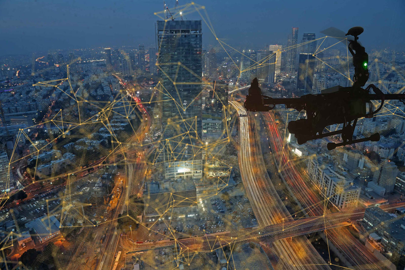 Drone flying over cityscape with cranes and construction at night, illuminated by lights.