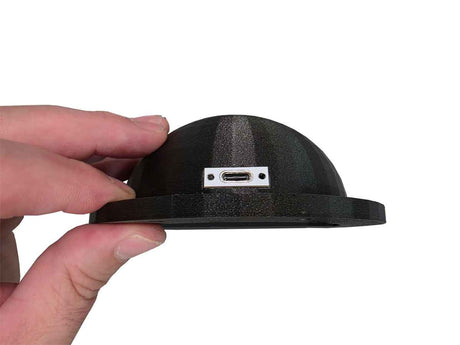 Black dome-shaped object with USB port held by a hand on a white background