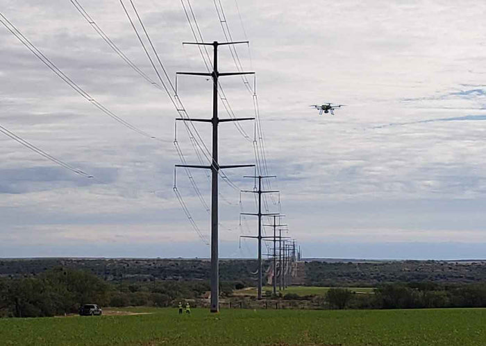 Power lines with a drone flying near them against a cloudy sky.