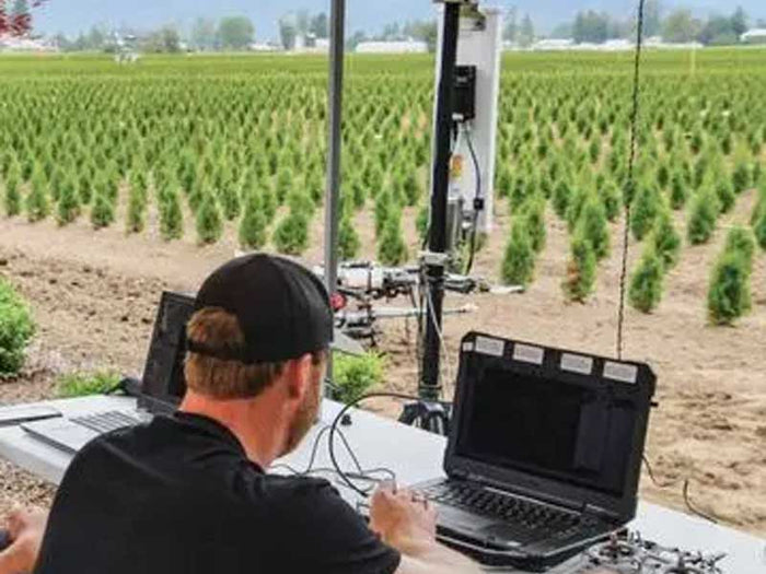 Person using a laptop in a field with agricultural equipment